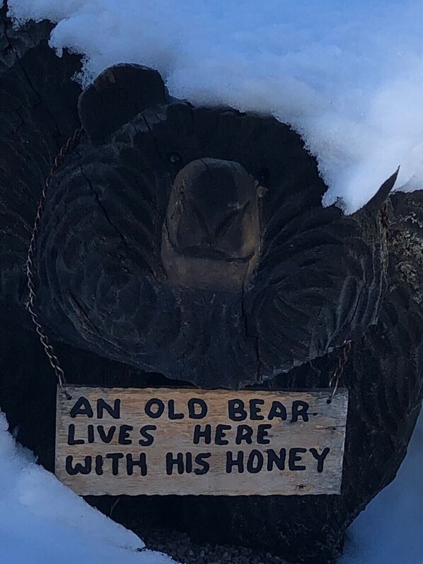 A wooden sign with a bear carving and text stating "AN OLD BEAR LIVES HERE WITH HIS HONEY".