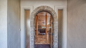 Ein steiner Torbogen führt in einen Raum mit Holzboden und Deckenventilator.