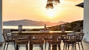 Un tavolo da pranzo con sei sedie in vimini, una bottiglia di vino e due bicchieri su un vassoio, con vista su un tramonto suggestivo.