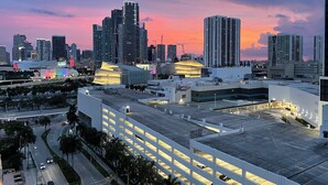 A modern cityscape with high-rise buildings and a large, illuminated building in the foreground. - Sunshine Miami Vacation ☀️ (Miami)
