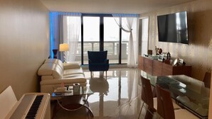 A modern hotel room with a piano, a sofa, a dining table with chairs, a TV, and a balcony with curtains. - Sunshine Miami Vacation ☀️ (Miami)