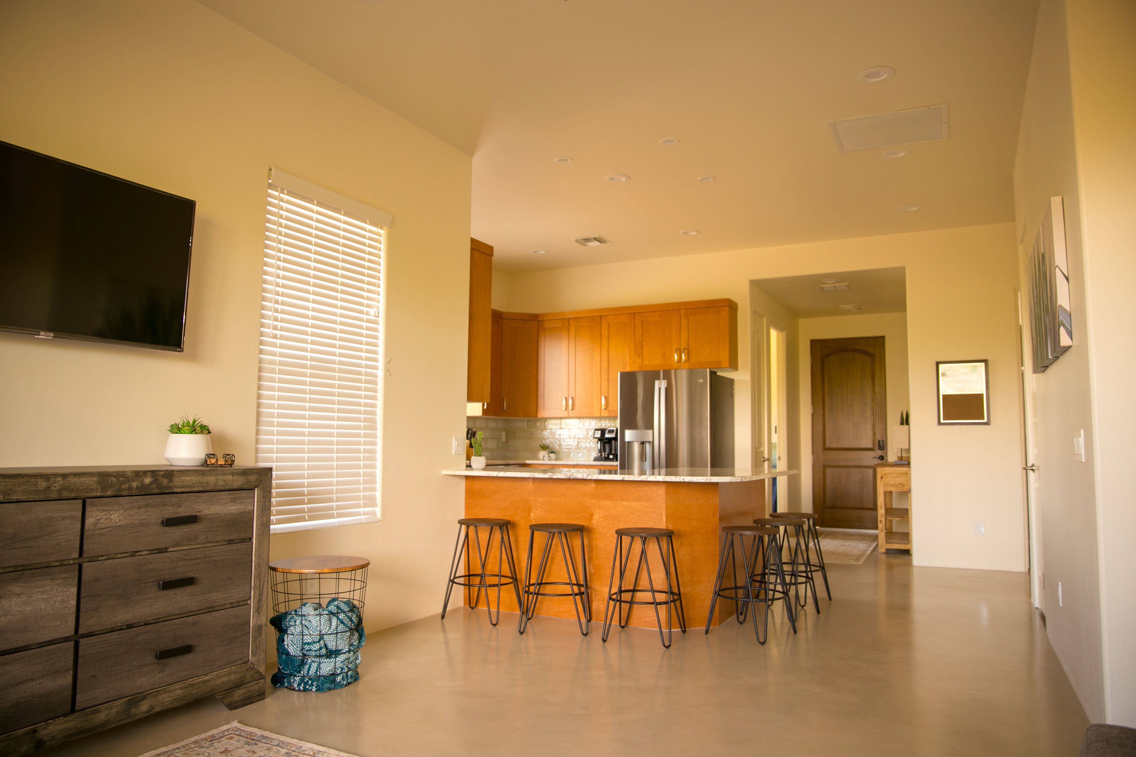 A modern kitchen with wooden cabinets, a stainless steel refrigerator, and a bar area with stools.