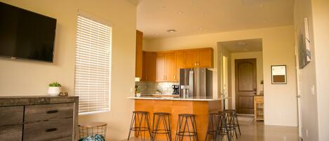 A modern kitchen with wooden cabinets, a stainless steel refrigerator, and a bar area with stools.