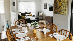 A dining area with a wooden table set for four, surrounded by wooden chairs. A vase with flowers is placed on the table.