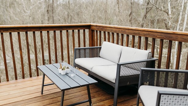 A wooden deck with a wicker sofa and two chairs, a small table, and a glass of water.
