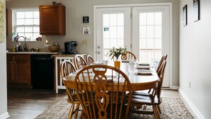 A dining area with a wooden table and chairs, a kitchen with wooden cabinets, and a window with blinds.