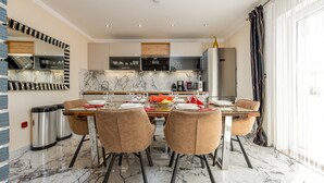 A modern dining area with a marble floor, a central table set for four, and a kitchen with built-in appliances in the background.