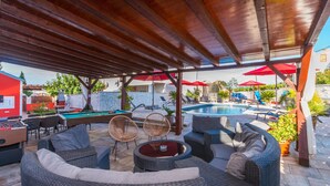 An outdoor lounge area with wicker furniture, a pool, and red umbrellas.