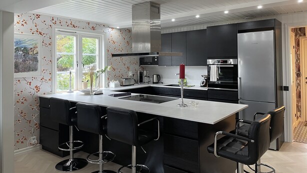 A modern kitchen with a central island, bar stools, a large refrigerator, and a window with a view of greenery. - Oas 300m ifrån centrum Uddevalla -  Bubbelpool uteplats (Västra Götalands län)