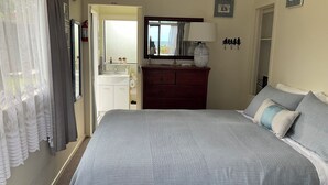 A bedroom with a large bed, a dresser, a mirror, and a window with curtains. - Beachside Studio close to cafes & wineries  (Eskdale)