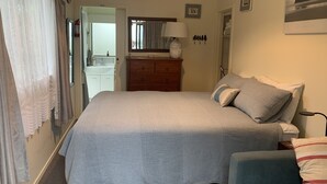 A bedroom with a bed, a dresser, a mirror, and a door leading to a bathroom. - Beachside Studio close to cafes & wineries  (Eskdale)