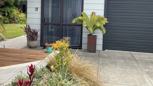 A modern house with a grey exterior, a black garage door, and a well-maintained garden with various plants and a wooden deck. - Beachside Studio close to cafes & wineries  (Eskdale)
