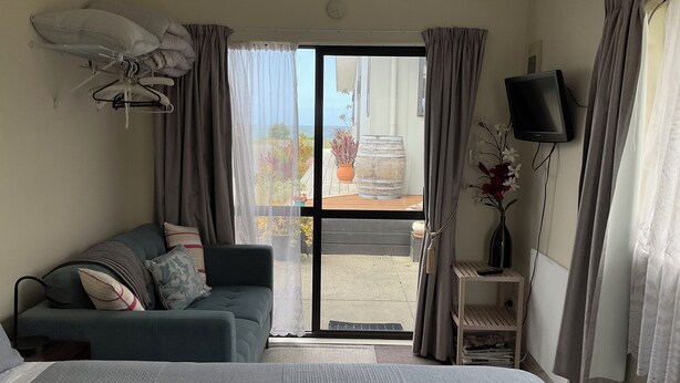 A hotel room with a bed, a sofa, a TV, and a view of the outside. - Beachside Studio close to cafes & wineries  (Eskdale)