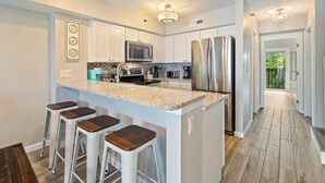 Une cuisine moderne avec des meubles blancs, des appareils en acier inoxydable et un îlot central doté de tabourets de bar.