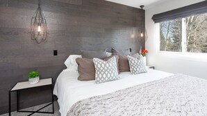 A modern bedroom with a large bed, dark wooden wall, and a window with a view of trees. - Ski, Hike, Bike out the door. Hot Tub, Hot Pools, Gym, Pickleball,Tennis Courts (Park City)