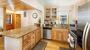 Une cuisine avec des meubles en bois, des plans de travail en granit, des appareils électroménagers en acier inoxydable et une horloge au mur.