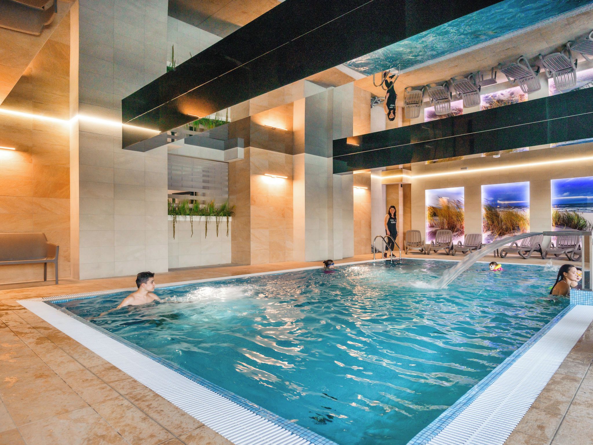 An indoor swimming pool with multiple lanes, a seating area with chairs, and a view of the sky through a large window.
