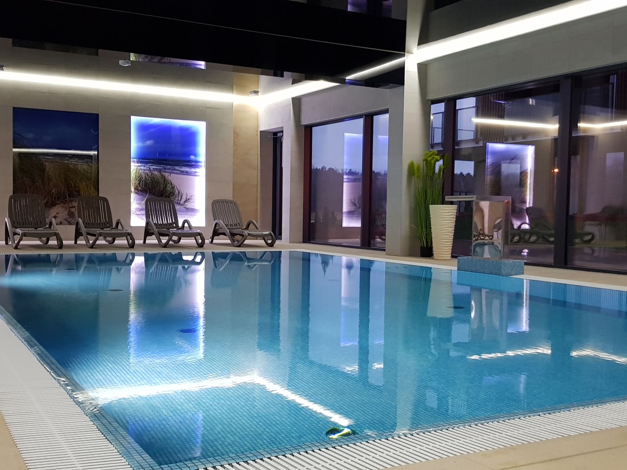 An indoor swimming pool with clear water, surrounded by lounge chairs and large windows with scenic views.