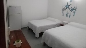 Ein Hotelzimmer mit zwei Betten, einem kleinen Tisch mit einer Pflanze, einem Kühlschrank und einem Wandbild mit Sternen und Seetang.