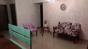 A living room with a teal bench, a purple armchair, a patterned sofa, a small table with a vase, and a clock on the wall. - HERMOSO DEPA CENTRO HISTORICO (Guadalajara)