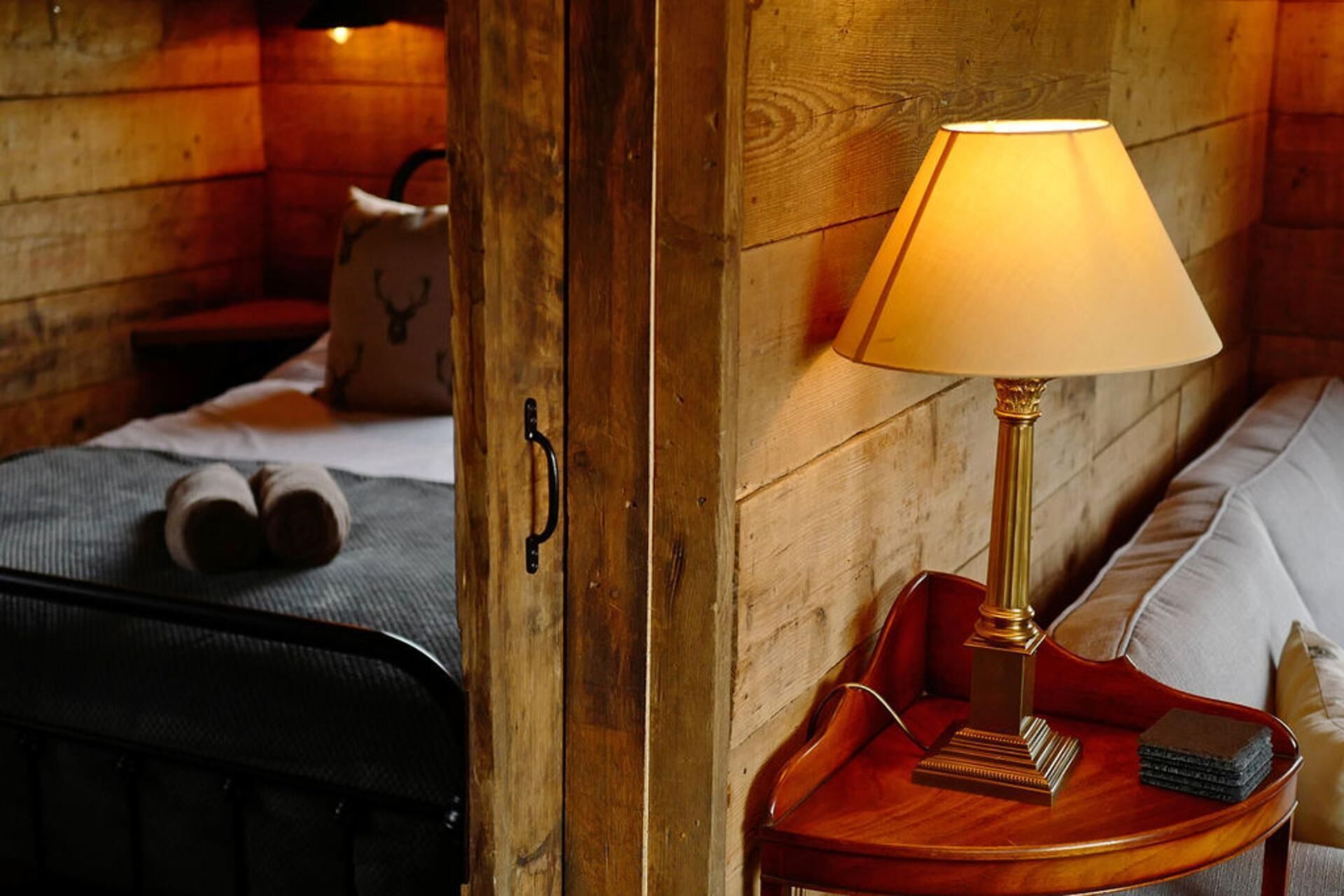 Et trægulvsrum med en seng, et sengebord med en lampe og en kuffert.