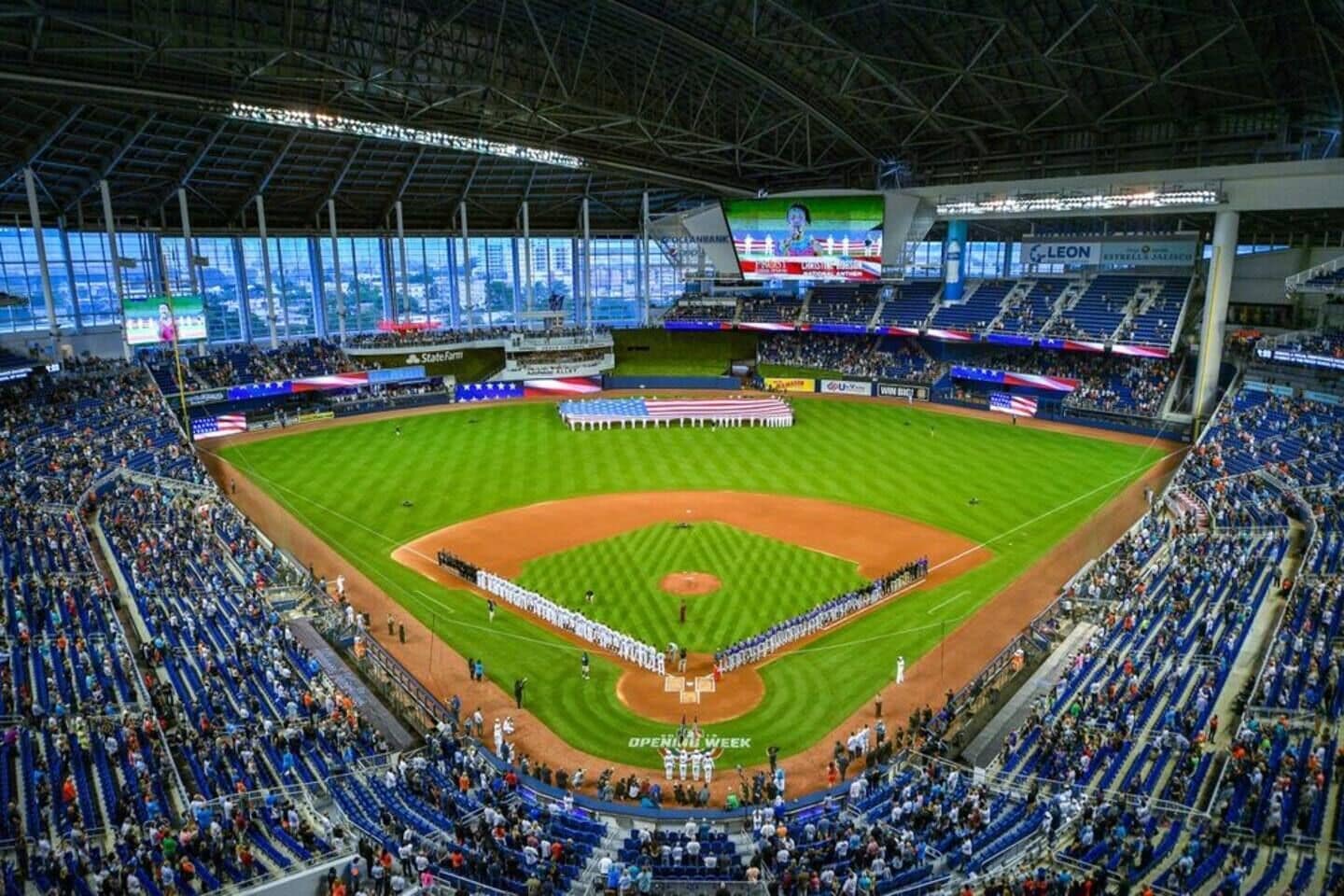 A large stadium with multiple tiers of seating, a central field, and a large screen displaying an event.