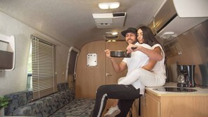 En kompakt indretning i en autocamper med et tekøkken, siddeområde og et vindue med plisségardiner.