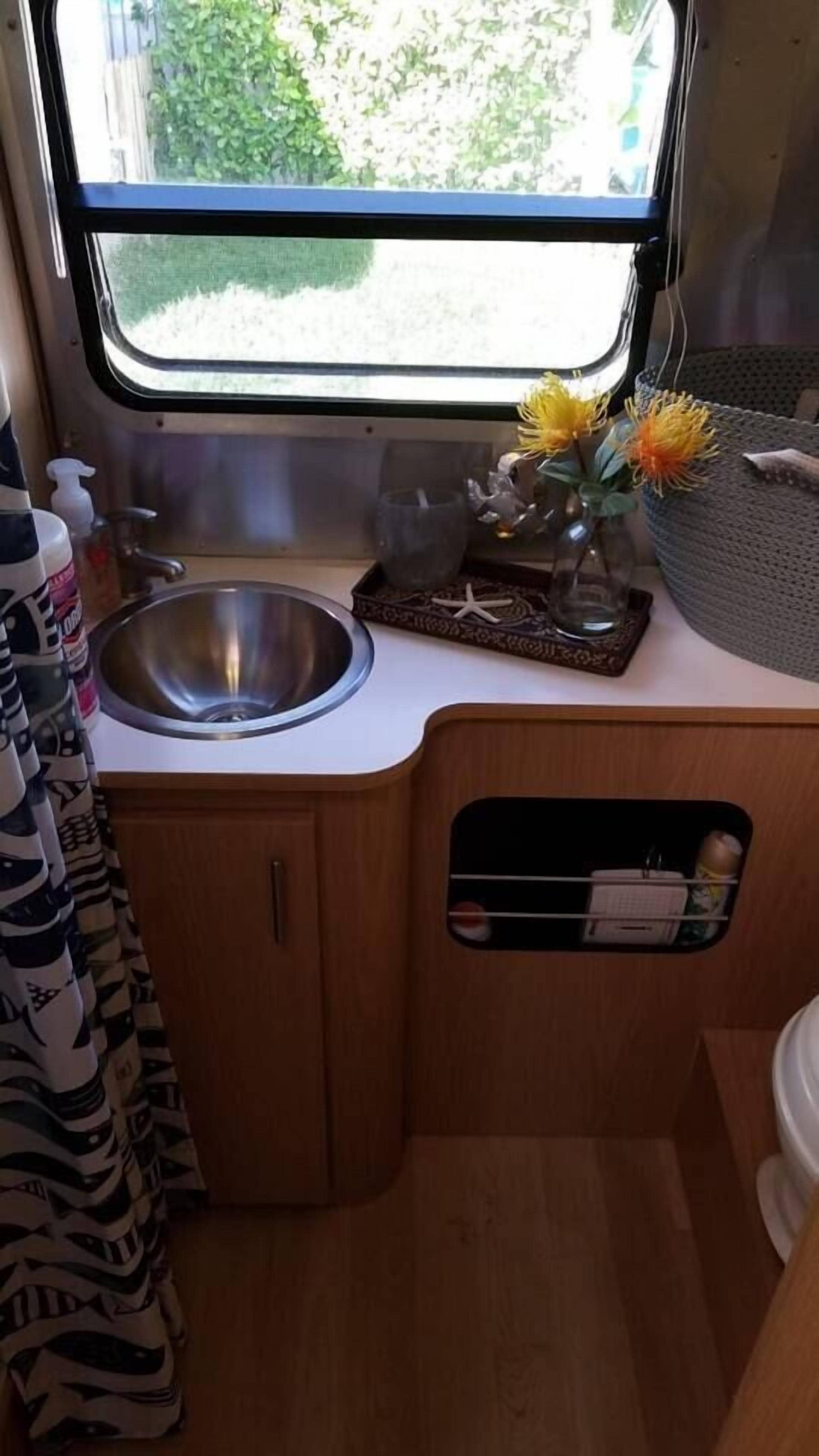 A compact kitchenette with a stainless steel sink, a small countertop, and a window with a view of greenery.
