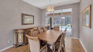 A dining room with a large wooden table, chairs, a chandelier, and a view of a swimming pool through large windows. - Spacious private pool home, close to beaches, with many upgrades! (Fort Myers)