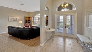 A spacious living area with a black sectional sofa, a round coffee table, and a bench. There are arched doorways and a chandelier. - Spacious private pool home, close to beaches, with many upgrades! (Fort Myers)