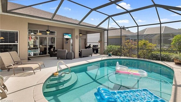 A covered outdoor swimming pool with lounge chairs, a hot tub, and a patio area with a view of the city. - Spacious private pool home, close to beaches, with many upgrades! (Fort Myers)