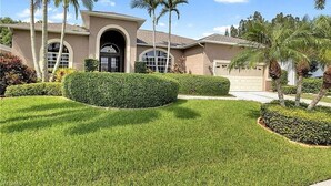 A residential house with a well-manicured lawn, palm trees, and a clear blue sky. - Spacious private pool home, close to beaches, with many upgrades! (Fort Myers)