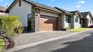 Ein modernes eingeschossiges Haus mit Naturstein-Fassade, einer großen Holztür zur Garage und einem gepflegten Rasen.