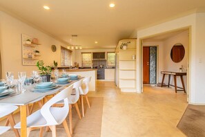 A modern kitchen with a dining area, featuring a central island, white chairs, and a buffet setup. - Iles Inn - Spa Pool, Pets OK, Walk to Forest (Rotorua)