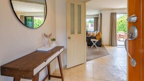 Ein Zimmer mit einem Holztisch, einem Spiegel und einer Tür zu einem Wohnbereich mit einer Couch und Vorhängen.