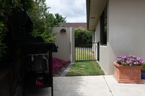 A backyard with a grill, a small lawn, a potted plant, and a gate leading to a house. - Iles Inn - Spa Pool, Pets OK, Walk to Forest (Rotorua)