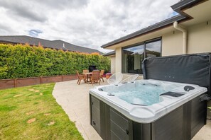 A hot tub in a backyard with a patio table and chairs, surrounded by a hedge and a house. - Iles Inn - Spa Pool, Pets OK, Walk to Forest (Rotorua)