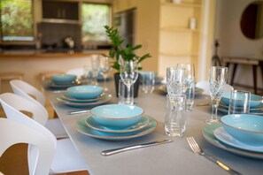 A dining table set with blue plates, clear glasses, and white chairs. - Iles Inn - Spa Pool, Pets OK, Walk to Forest (Rotorua)
