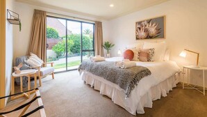 Ein modernes Schlafzimmer mit einem großen Bett, einer Sitzecke mit Stuhl und Tisch und Blick ins Freie durch eine Schiebetür.