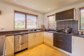 A modern kitchen with stainless steel appliances, dark cabinetry, and large windows with blinds. - Iles Inn - Spa Pool, Pets OK, Walk to Forest (Rotorua)