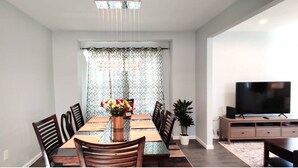 A dining area with a wooden table, chairs, a vase with flowers, and a TV on a stand.