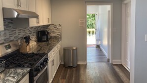A modern kitchen with white cabinets, a stainless steel range hood, a coffee maker, and a trash can.