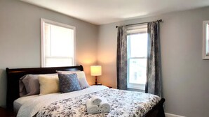 A bedroom with a bed, two windows, a lamp, and a wall outlet.