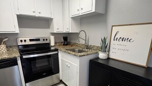 A kitchen with white cabinets, a stainless steel stove, a granite countertop, a black cabinet, and a framed quote on the wall.