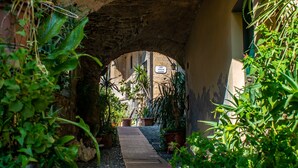 An arched passageway with a cobblestone path, surrounded by lush greenery and potted plants. - Ca Veggia for Nature Lovers with Views & Garden, Stellanello, Italy (Stellanello)