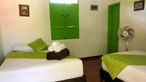 A hotel room with two beds, green curtains, a fan, and a small painting on the wall. - Room with 2 double beds (COMBIA)