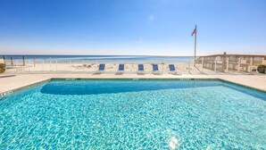 Une piscine d’un bleu éclatant, avec vue sur l’océan, un drapeau et un espace clos agrémenté de chaises longues.