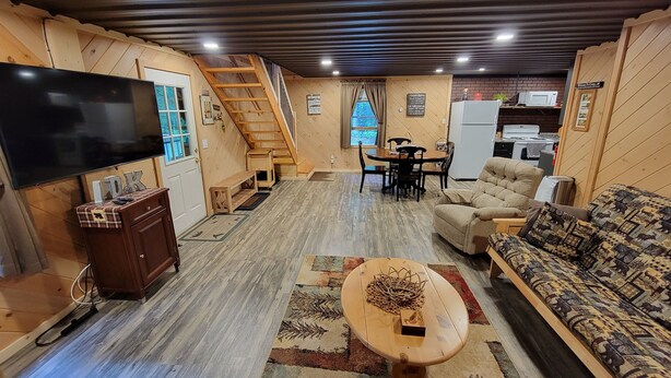 A cozy living room with a TV, sofa, and coffee table. A staircase leads to a dining area with a table and chairs.