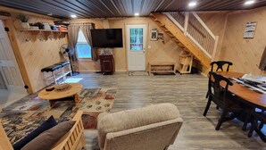 A cozy, wooden-furnished living room with a sofa, a dining table, and a staircase leading to an upper level.