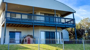 Un edificio moderno de dos pisos con techo curvo, balcón cubierto y patio cercado.